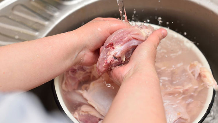 woman washes chicken in the sink